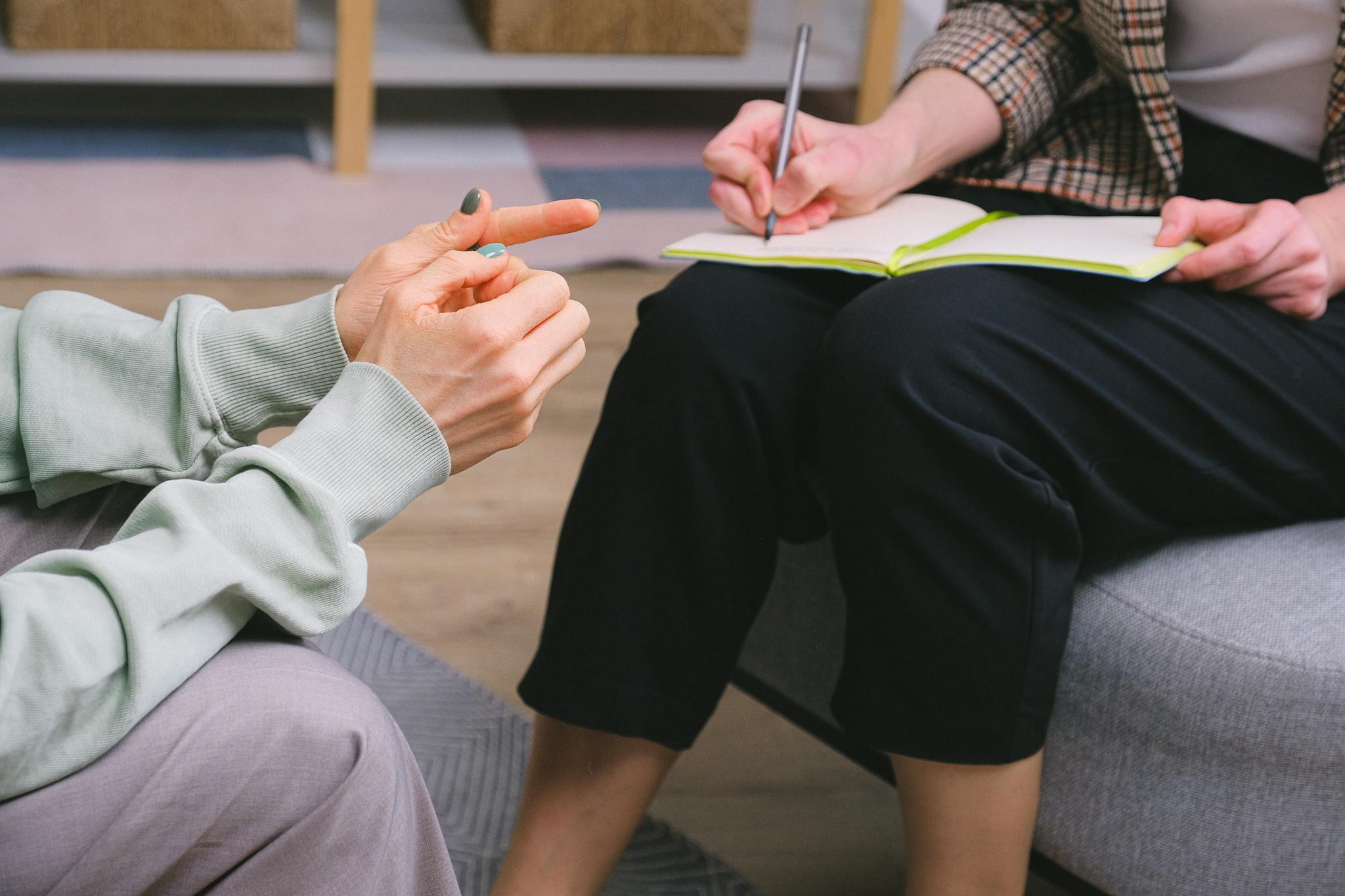 Crop anonymous female psychologist in formal outfit taking notes in copybook while sitting in armchair during session with unrecognizable patient