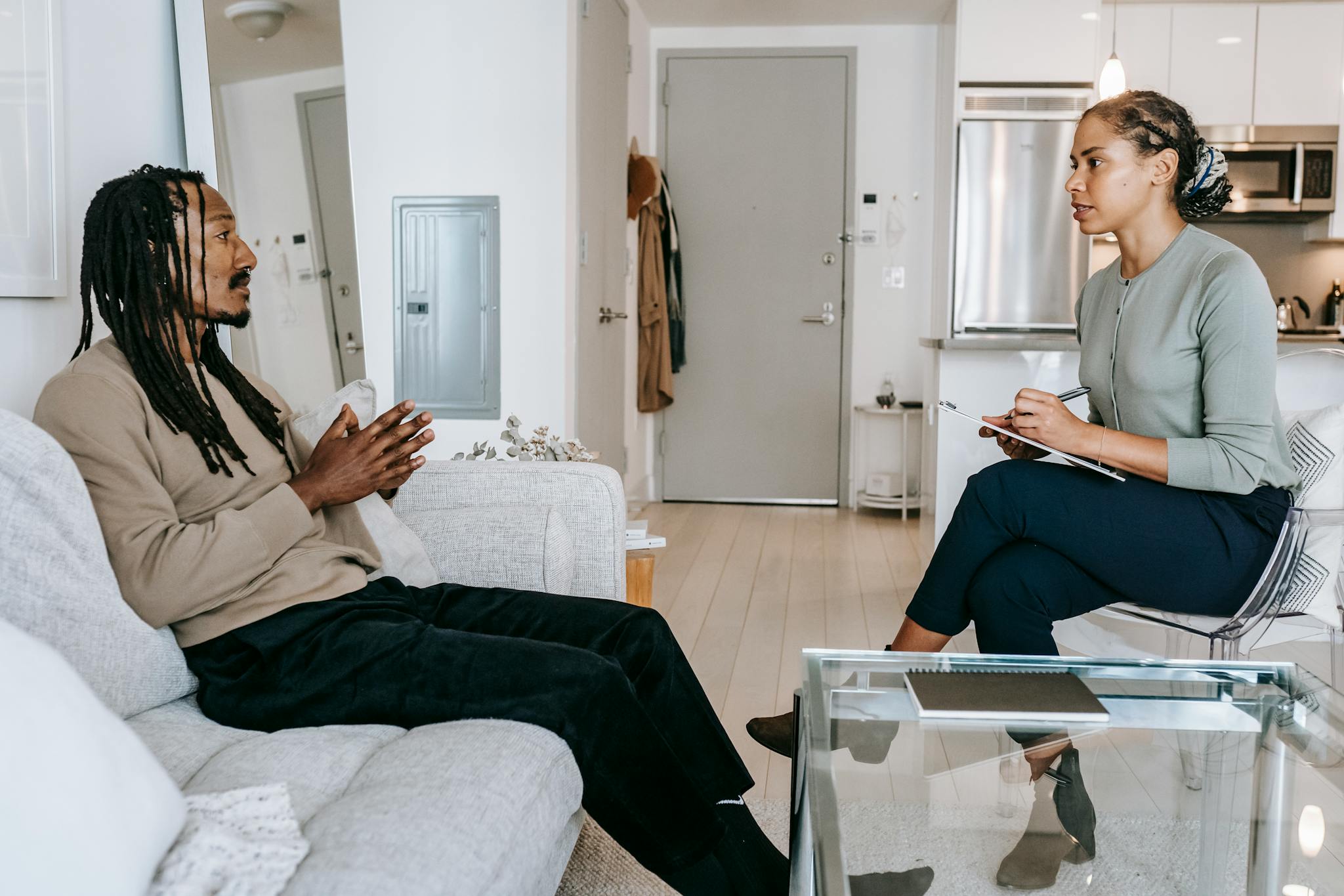 Side view of African American female therapist with crossed legs and clipboard taking notes while sitting in front of black male patient